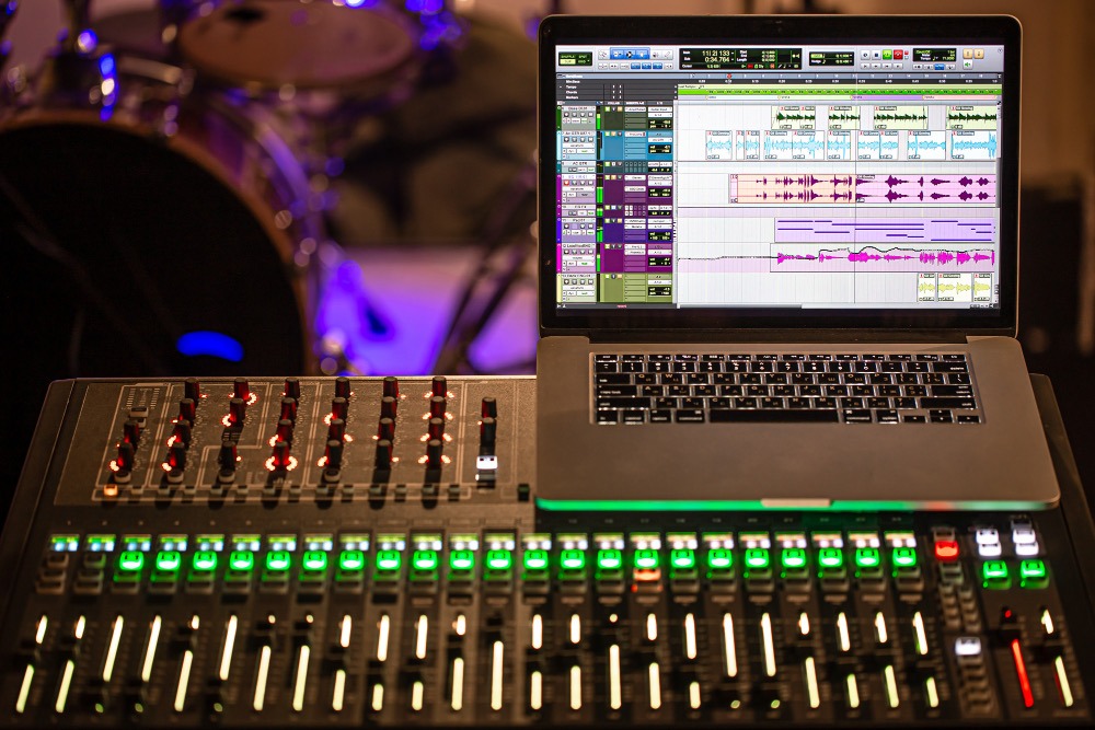 Analog mixing desk with a laptop showing multitrack audio waveforms