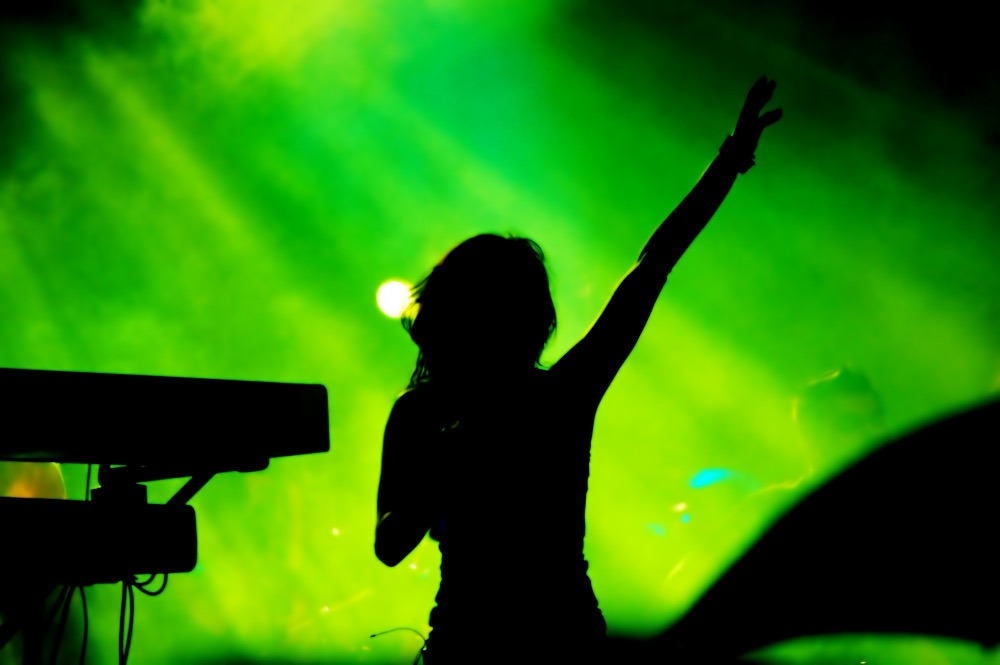 DJ raising an arm on stage under audio-reactive green stage lights